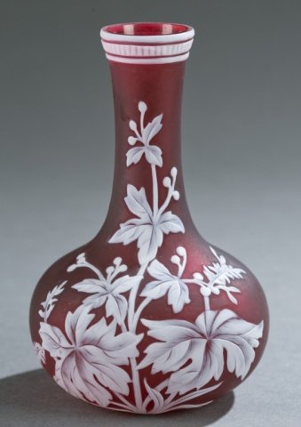 Small cameo art glass vase, Webb style, 19th c.: A small cameo art glass vase. In the style of Thomas Webb & Sons. English. Late 19th century. Unmarked. With deep red body and cut white overlay of plant motif and repeating line pattern at top. 5 1/2