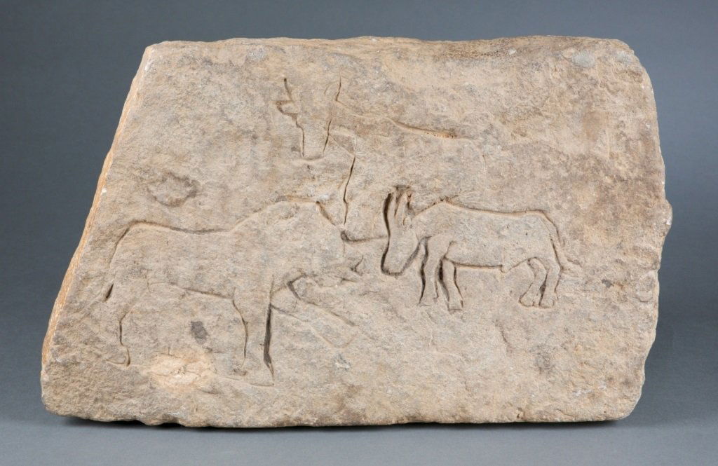 A relief carved stone.: A rectangular shaped stone with carved three animals in profile. Provenance: The Inventory and Collection from the Estate of Merton D. Simpson.