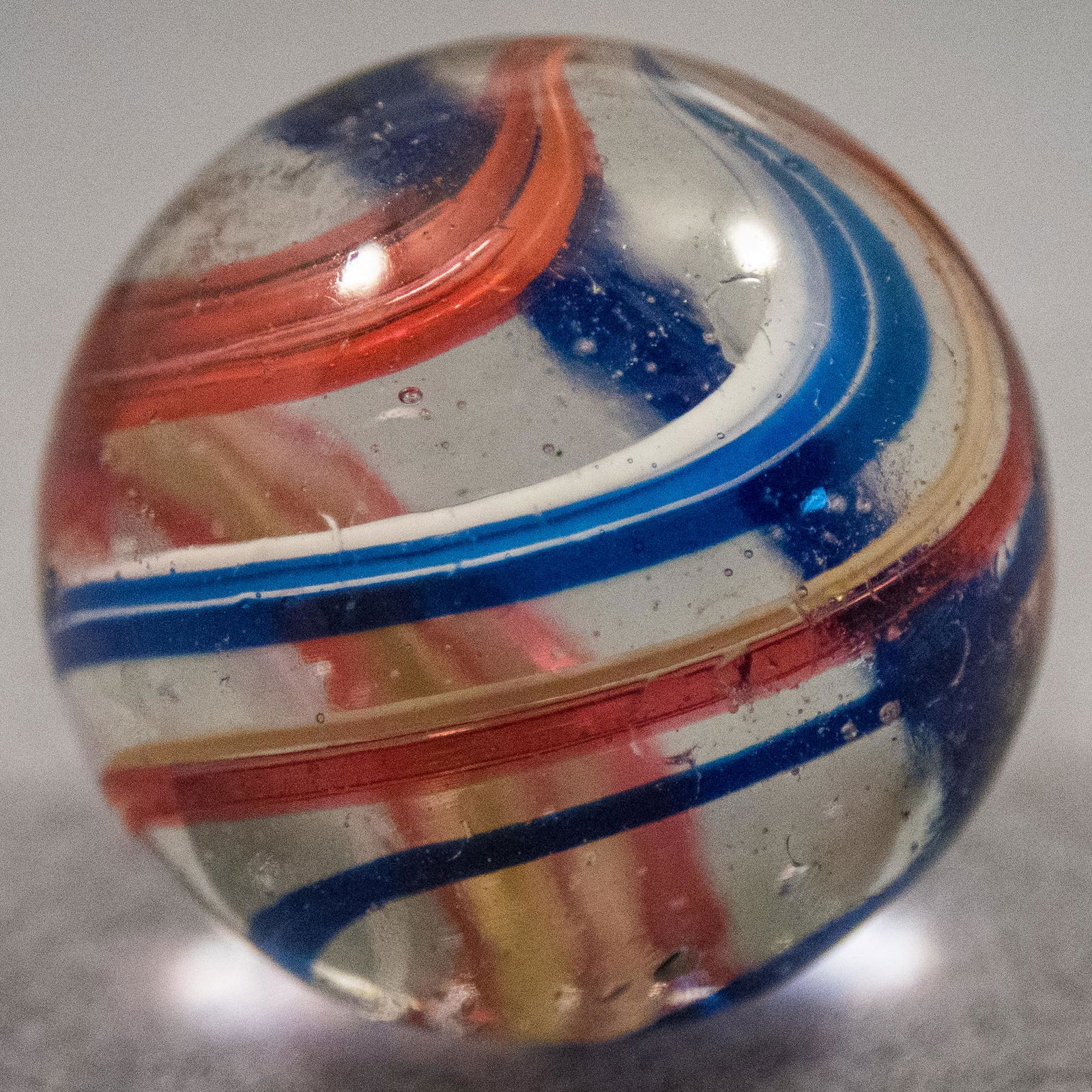 Marbles: SWIRL, Coreless. 29/32". Polished: SWIRL, Coreless. Clear base. No inner core. Subsurface layer is five bands. Three are blue on white. Two are pink on yellow. Another pink on yellow is missing. Reverse twist top. Germany, circa 1860-1