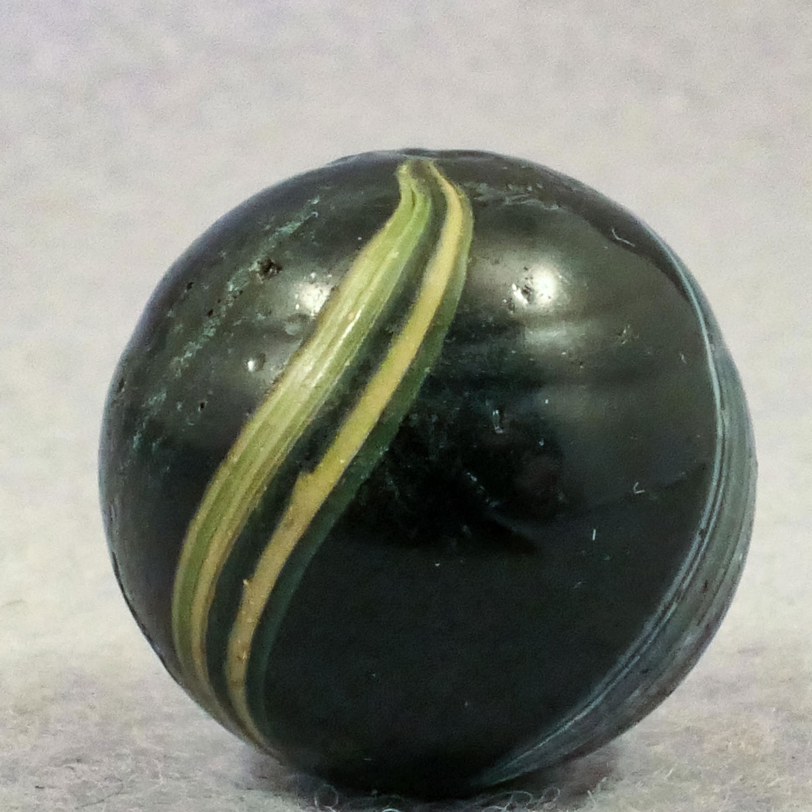 Marbles: OTHER HANDMADE, Indian. 11/16". Mint(-) (9.0).: OTHER HANDMADE, Indian. Opaque black base. Two bands covering about sixty percent of the surface. One is very wide and is stretched white and green. Other is stretched yellow. One melt chip. Germany,