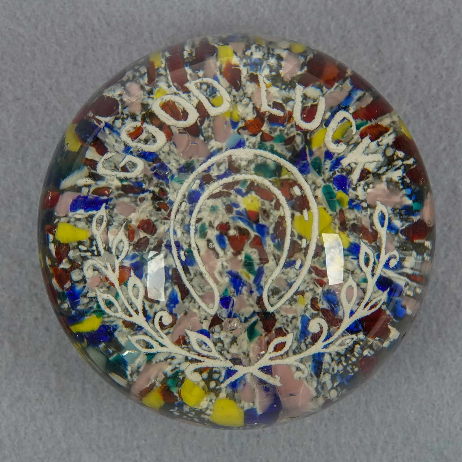 PAPERWEIGHT, American. Good Luck.: PAPERWEIGHT, American. Crimped frit base. Floating above that in white frit is "Good Luck" with a horseshoe and a garland. Unidentified manufacturer, probably South Jersey. Circa late 1800s, early 190
