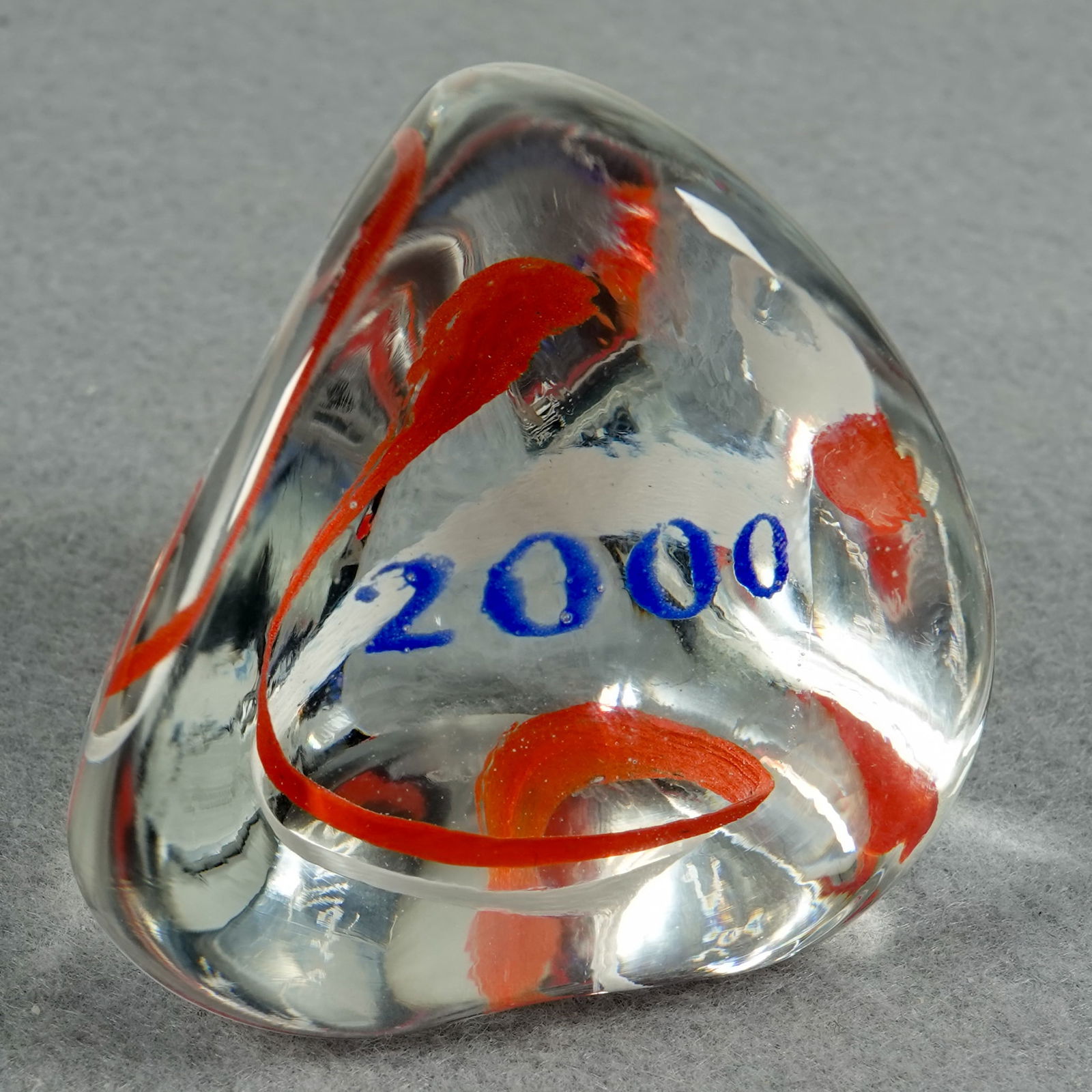 PAPERWEIGHT, Caithness Glass. Millenium Pebble.: PAPERWEIGHT, Caithness Glass. Millenium Pebble. A Caithness Pebble weight with "2000" in blue frit in it. Signed on bottom "Millenium Pebble Caithness Scotland". 2-1/8" width, 2-1/4" height. Mint.