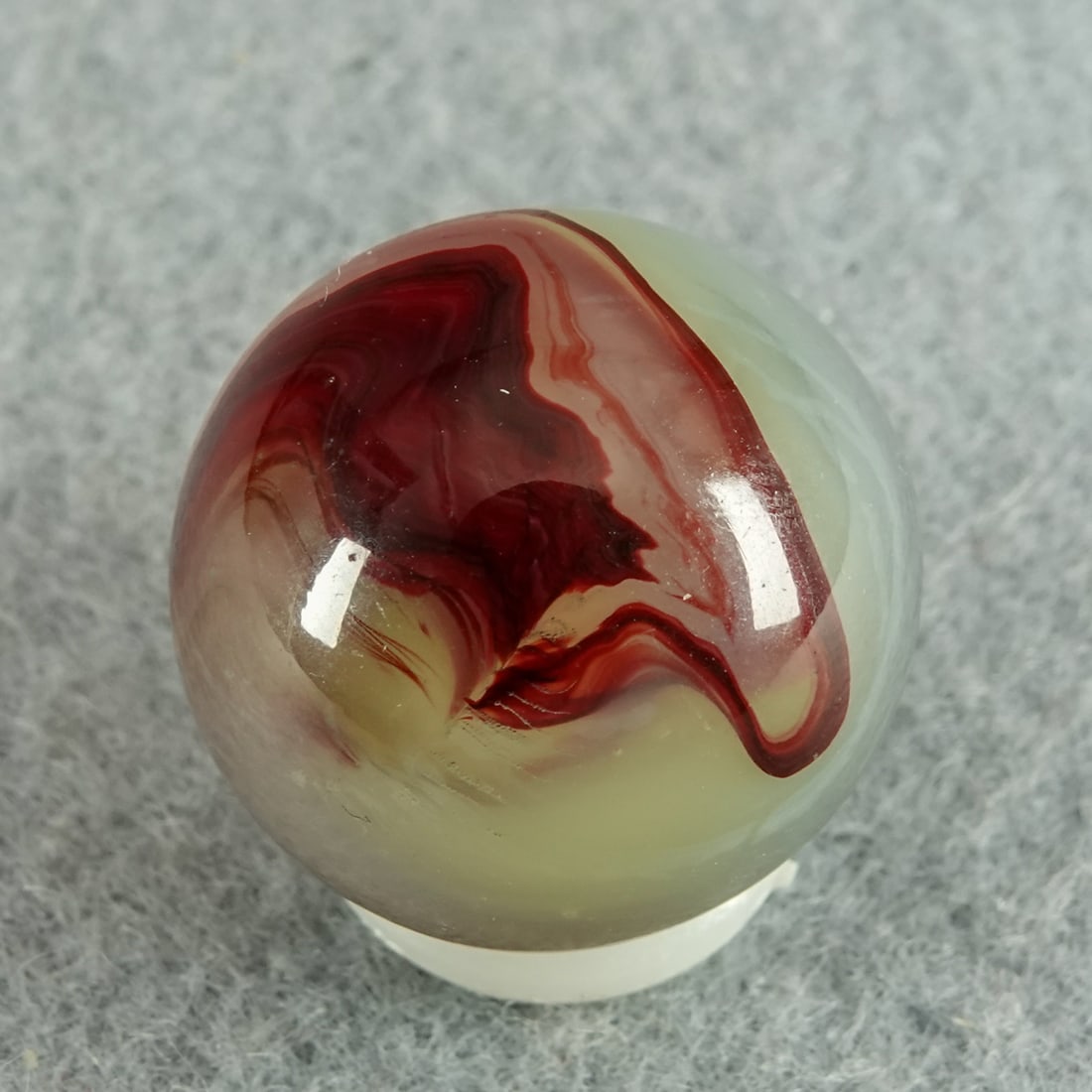 AKRO AGATE COMPANY, Lemonade Oxblood. 23/32". Mint (9.9).: AKRO AGATE COMPANY, Lemonade Oxblood. An odd Lemonade Oxblood. The base is not the traditional green-tinted Ade base, but rather a milky white with a slight green tint, but still fluorescent. Wispy wh