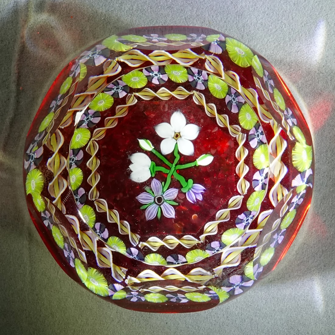 PAPERWEIGHT, Perthshire Paperweights.: PAPERWEIGHT, Perthshire Paperweights. Annual line paperweight. Beautiful flowers on red flash base. Has a "P 1986" date cane in the base. Faceted. 3" wide, 1-7/8" tall .