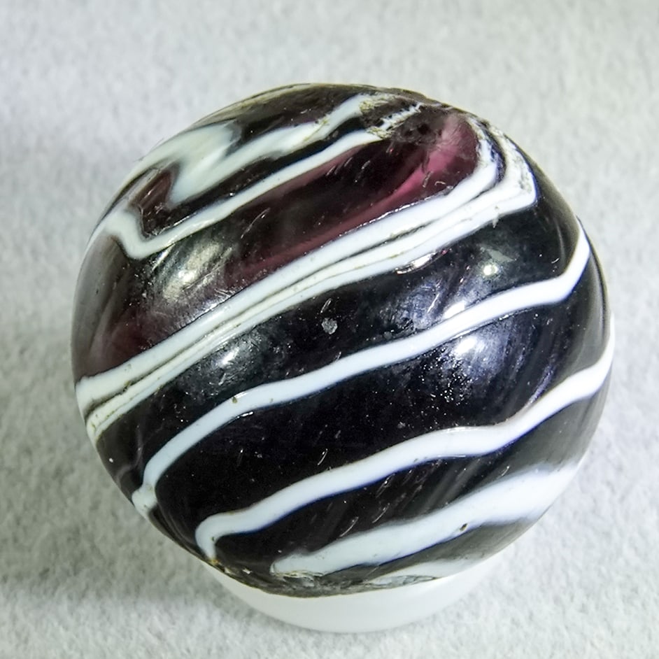 OTHER HANDMADE, Slag. 23/32". Mint (9.7).: OTHER HANDMADE, Slag. Two-pontil marble. Very dark purple base with opaque white marbrie loopings on the surface. Hard to find. Germany, circa 1860-1920. Previously sold in Block's Marble Auction Apri