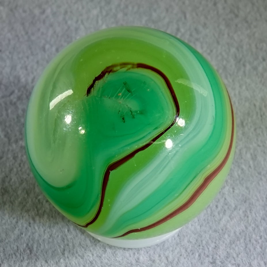 AKRO AGATE COMPANY, Limeade Oxblood. 3/4". Mint (9.9).: AKRO AGATE COMPANY, Limeade Oxblood. Shooter Limeade Corkscrew with a oxblood spiral next the the green. Fluorescent. Clarksburg WV, circa 1925-1935. 3/4". Mint (9.9).