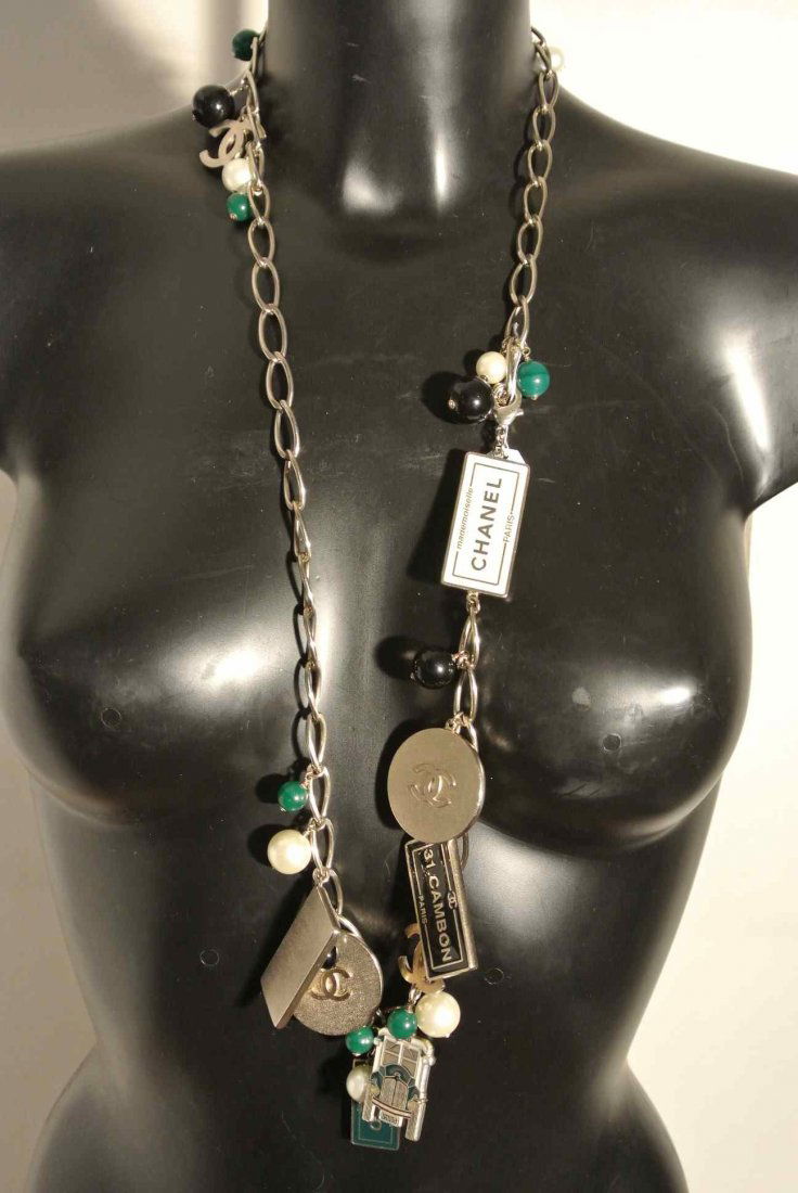 CHANEL Ceinture/sautoir en métal light gold alternée de: CHANEL Ceinture/sautoir en métal light gold alternée de "Charms" au logo de la marque et de perles fantaisies vertes, blanches et noires - Longueur : 91 cm - Length : 35,8 in (très bon état/very g