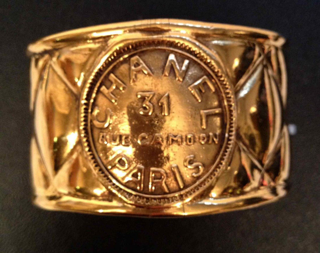 CHANEL Bracelet manchette en métal doré matelassé orné : CHANEL Bracelet manchette en métal doré matelassé orné d'un médaillon siglé - Largeur : 4 cm - Width : 1,5 in. (bon état, petite fêlure intérieur/good condition, one tiny crack inside)