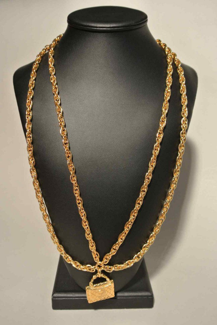 CHANEL Long collier en métal doré à double chaines, ret: CHANEL Long collier en métal doré à double chaines, retenant un pendentif sac 2 55 - Hauteur : 39 cm - Height : 15,3 in. (très bon état/very good condition)