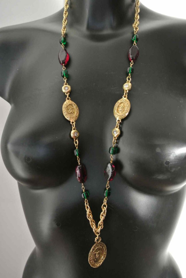 CHANEL Long collier en métal doré alterné de perles de : CHANEL Long collier en métal doré alterné de perles de verre vertes, pâte de verre rouge, strass et médaillons siglés et gravés Coco Chanel - Hauteur : 47 cm - Height : 18,5 in. (très bon éta