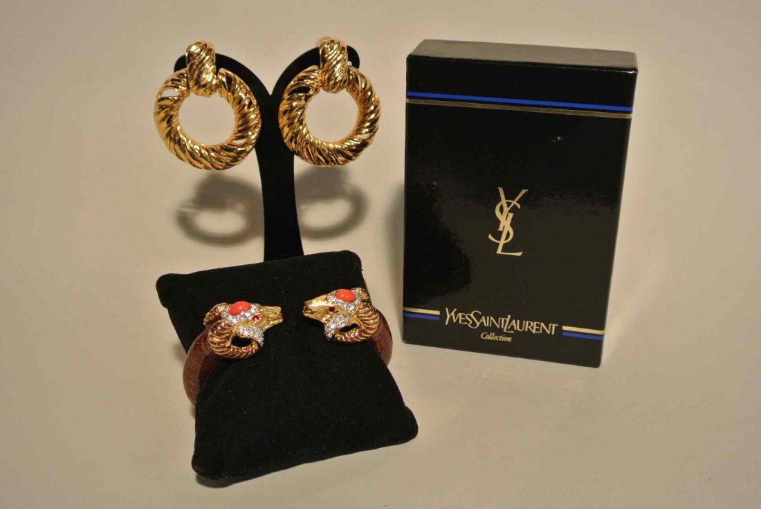 YVES SAINT LAURENT Paire de clips d'oreilles anneaux en: YVES SAINT LAURENT Paire de clips d'oreilles anneaux en métal doré, on y joint un bracelet émaillé KENNETH JAY LANE orné de têtes de bélier - Hauteur des clips : 5,5 cm - Height of the earclips