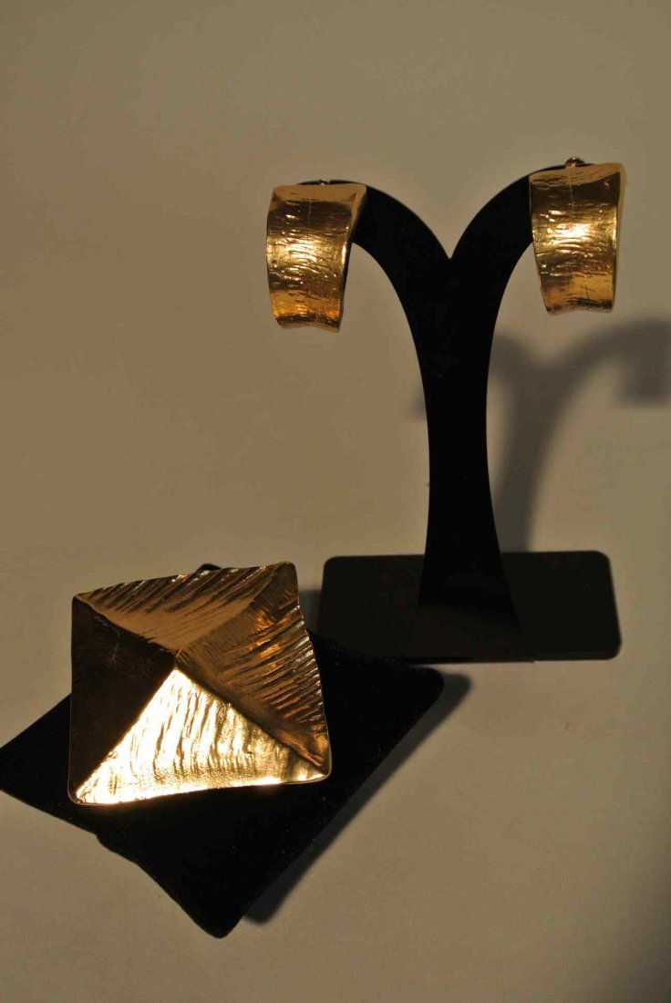 YVES SAINT LAURENT Lot composé d'une broche/pendentif p: YVES SAINT LAURENT Lot composé d'une broche/pendentif pyramide et d'une paire de clips d'oreilles anneaux en métal doré - Hauteur de la broche : 6 cm et hauteur des clips 3 cm / Height of the brooc