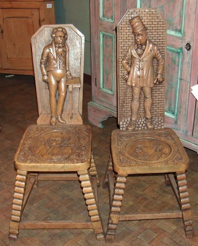 A PAIR OF ENGLISH PICKLED ELM HALL CHAIRS, late 19: A PAIR OF ENGLISH PICKLED ELM HALL CHAIRS, late 19th century. With characters from Charles Dicken's writings on the back, the seats with figural medallions, splayed legs - 41 in. x 14 in. x 15 in.