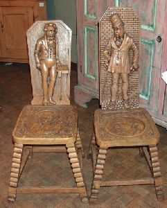 A PAIR OF ENGLISH PICKLED ELM HALL CHAIRS, late 19: A PAIR OF ENGLISH PICKLED ELM HALL CHAIRS, late 19th century. With characters from Charles Dickens' writings on the back, the seats with figural medallions, splayed legs - 41 in. x 14 in. x 15 in.