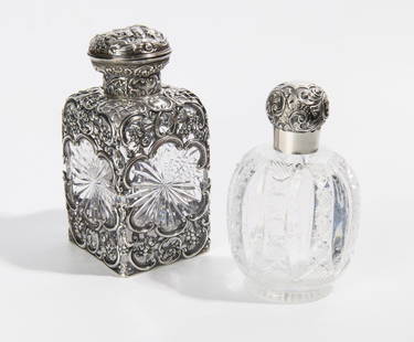 TWO ENGLISH VICTORIAN STERLING SILVER MOUNTED COLORLESS CUT CRYSTAL VANITY BOTTLES. One, square: TWO ENGLISH VICTORIAN STERLING SILVER MOUNTED COLORLESS CUT CRYSTAL VANITY BOTTLES. One, square sided with ornate pierced silver overlay cast with flowerheads and C-scrolls, H: 16 in.; one, footed,