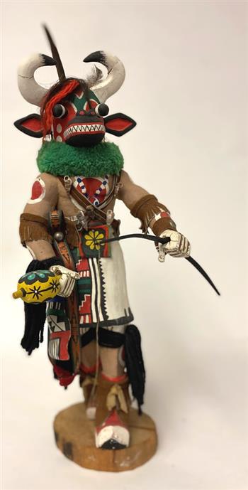 HOPI PUEBLO WAKAS (COW) KATSINA DOLL. 20th Century. - Height with base: 20".: HOPI PUEBLO WAKAS (COW) KATSINA DOLL. 20th Century. Hand carved of cotton wood doll, signed "Vic M." on the bottom. Katsina doll with great detail, decorated with fur and seashells. - Height with base