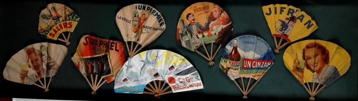 NINE FRENCH FOLDING PAPER LITHOGRAPHED ADVERTISING FANS ARRANGED IN A SHADOW BOX FRAME,