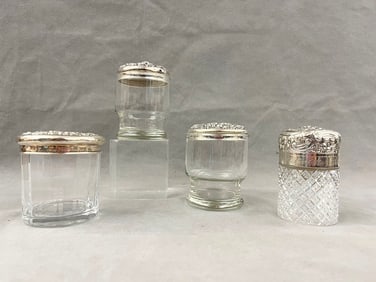 FOUR ASSORTED CYLINDRICAL GLASS VANITY JARS WITH STERLING SILVER FLORAL REPOUSSE COVERS, late
