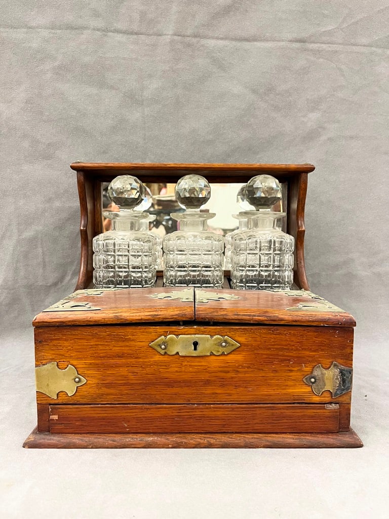 BRASS-MOUNTED WALNUT TANTALUS WITH SET THREE SQUARE-SIDED CUT CRYSTAL DECANTERS, 19th century. - H:: BRASS-MOUNTED WALNUT TANTALUS WITH SET THREE SQUARE-SIDED CUT CRYSTAL DECANTERS, 19th century. Mirrored back-panel; hinged bisected front section opens to five compartments. - H: 12 3/4 in.; W: 14 in.