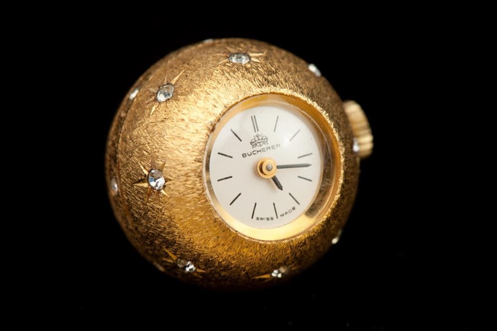 LADY'S BUCHERER YELLOW GOLD-PLATED TEXTURED ORB-FORM PENDANT WATCH. - D: 3/4 in.: LADY'S BUCHERER YELLOW GOLD-PLATED TEXTURED ORB-FORM PENDANT WATCH. Florentined case overall gypsy-set with numerous round faux diamonds; white enamel dial with black enamel bars for numerals. - D: 3