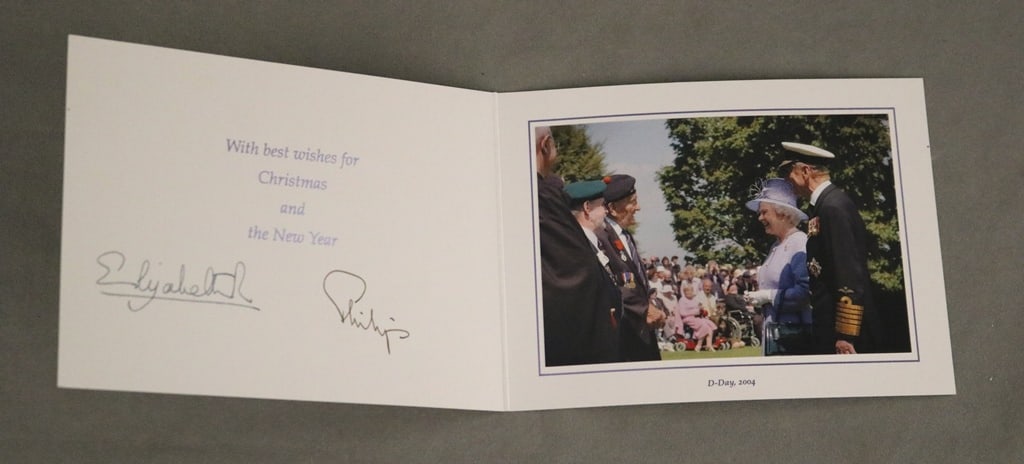 H.M. QUEEN ELIZABETH II AND H.R.H. THE DUKE OF EDINBURGH, SIGNED 2004 CHRISTMAS CARD WITH COLOR: H.M. QUEEN ELIZABETH II AND H.R.H. THE DUKE OF EDINBURGH, SIGNED 2004 CHRISTMAS CARD WITH COLOR PHOTOGRAPH OF D-DAY. With twin gilt Royal cyphers to cover, color photograph on the interior of The Quee