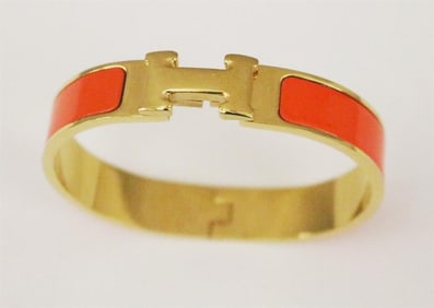 SIGNED HERMES/MADE IN FRANCE YELLOW-GOLD PLATED AND ORANGE ENAMEL HINGED OVAL "H" LOGO BRACELET,