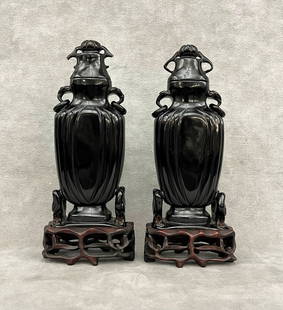 PAIR CHINESE-INSPIRED ART DECO BLACK BAKELITE TWO-HANDLE, LIFT-COVER VASES. - H: Vases, 7 1/8".: PAIR CHINESE-INSPIRED ART DECO BLACK BAKELITE TWO-HANDLE, LIFT-COVER VASES. Carved teakwood fitted stands. (One with damaged handles). - H: Vases, 7 1/8".