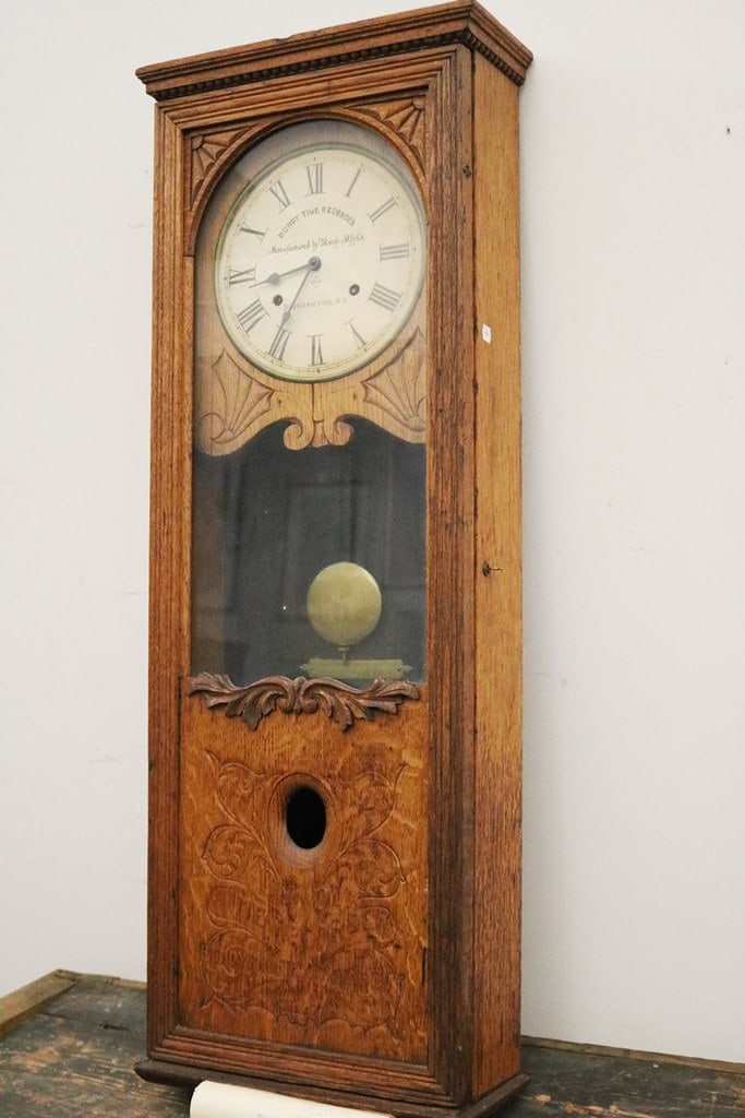 BUNDY CO. TIME RECORDER PENDULUM WALL CLOCK, late 19th century. - H; 44 1/2 in. W: 16 1/4 in. D: 6: BUNDY CO. TIME RECORDER PENDULUM WALL CLOCK, late 19th century. Vertical carved oak case with glazed door; face with Roman numerals - H; 44 1/2 in. W: 16 1/4 in. D: 6 1/2 in.