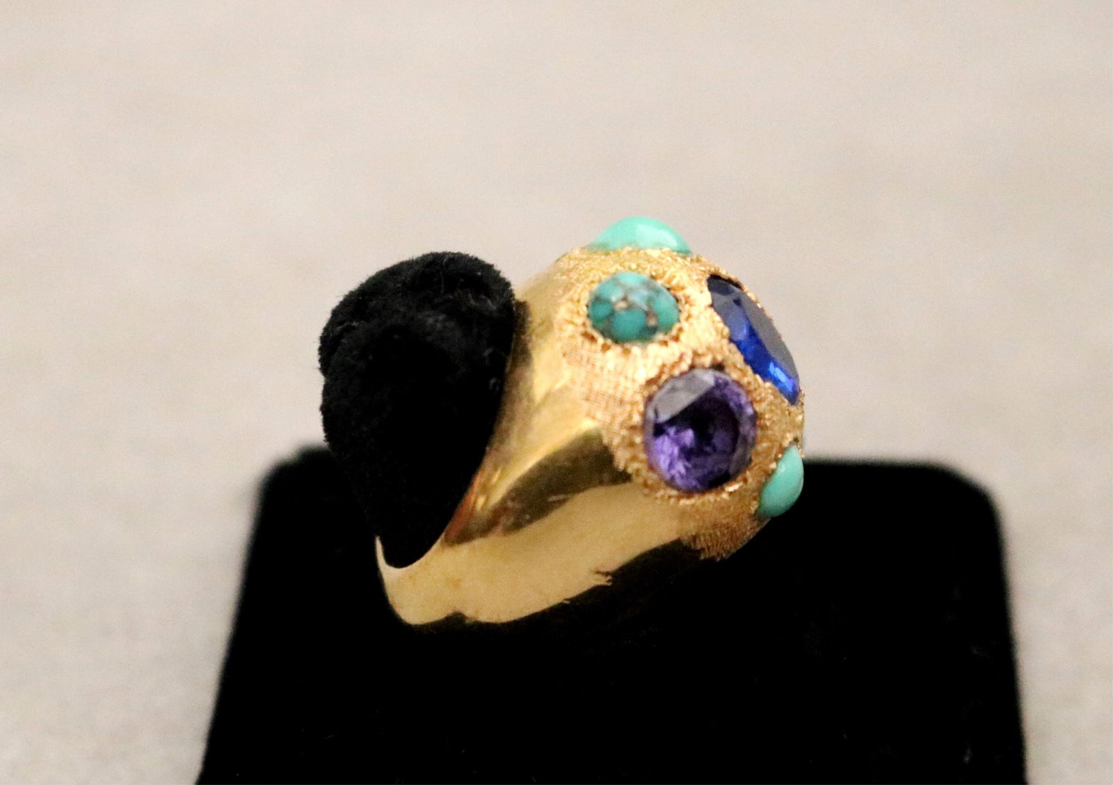 EGYPTIAN YELLOW GOLD TEXTURED AND SMOOTH-POLISHED GOLD DOME RING SET WITH OVAL BLUE FAUX GEMSTONE: EGYPTIAN YELLOW GOLD TEXTURED AND SMOOTH-POLISHED GOLD DOME RING SET WITH OVAL BLUE FAUX GEMSTONE (WORN SURFACE), FOUR TURQUOISE CABOCHONS AND TWO AMETHYSTS.Ring size 5. Gross wt.: 6 dwt.