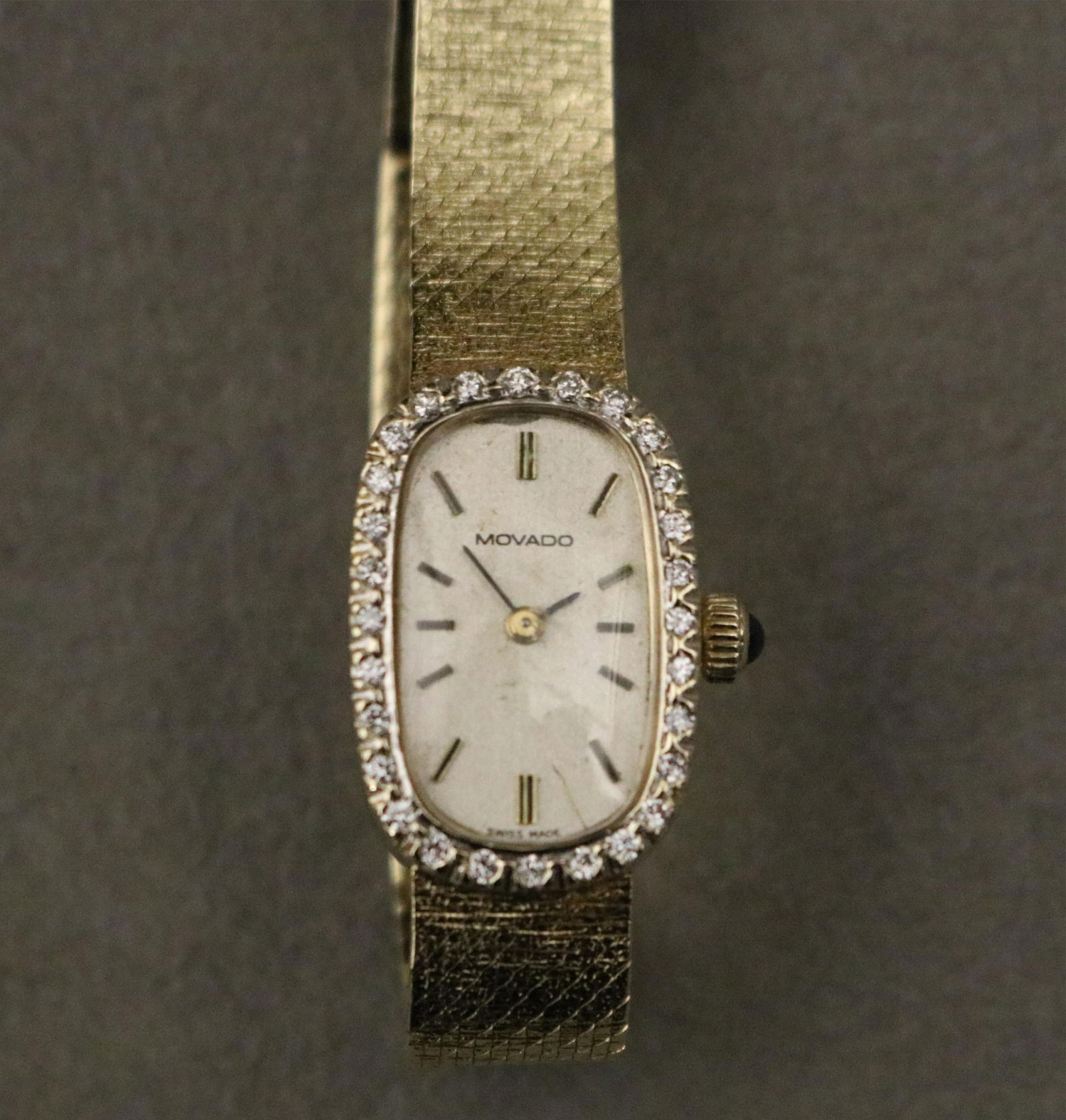 LADY'S MOVADO 14K YELLOW GOLD AND AND DIAMOND WRISTWATCH L: 6 1/2 in. Gross wt.: 14 dwt.: LADY'S MOVADO 14K YELLOW GOLD AND AND DIAMOND WRISTWATCHOblong case surrounded by 28 brilliant-cut round diamonds; silvered enamel face with bars for numerals; integrated tapering florentined mesh fle