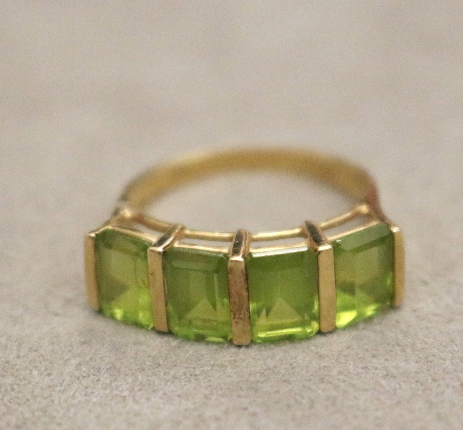 14K YELLOW GOLD AND PERIDOT RING - Ring size: 7 3/4.: 14K YELLOW GOLD AND PERIDOT RING Row of four matched bar-set, vertically oriented, emerald-cut peridots Ring size: 7 3/4