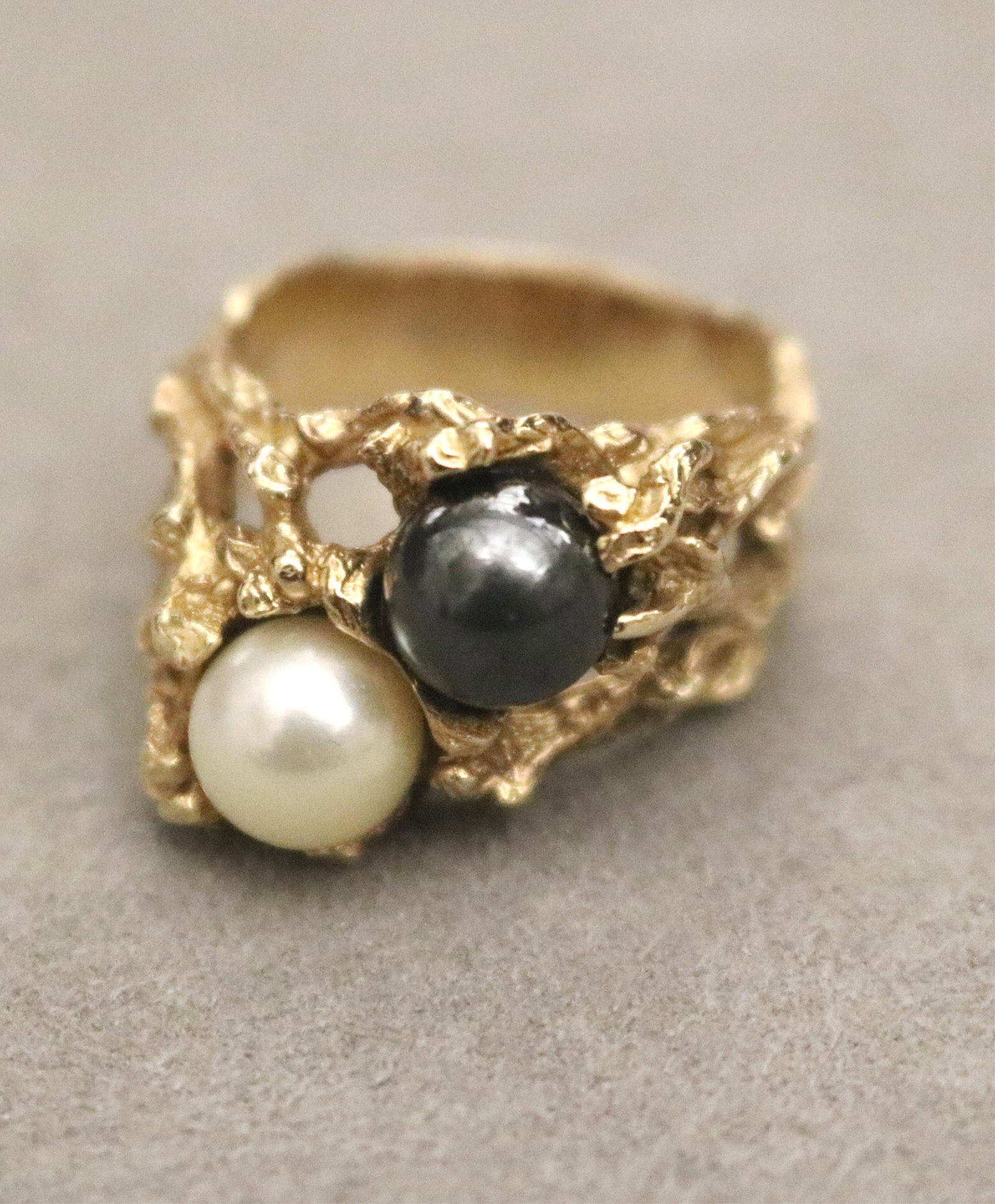14K TEXTURED YELLOW GOLD AND BLACK AND WHITE CULTURED PEARL RING - Ring size: 8. Gross wt. 9 dwt.: 14K TEXTURED YELLOW GOLD AND BLACK AND WHITE CULTURED PEARL RING One 7mm black pearl with one 7mm white pearl set diagonally in openwork branch design setting. Ring size: 8. Gross wt. 9 dwt