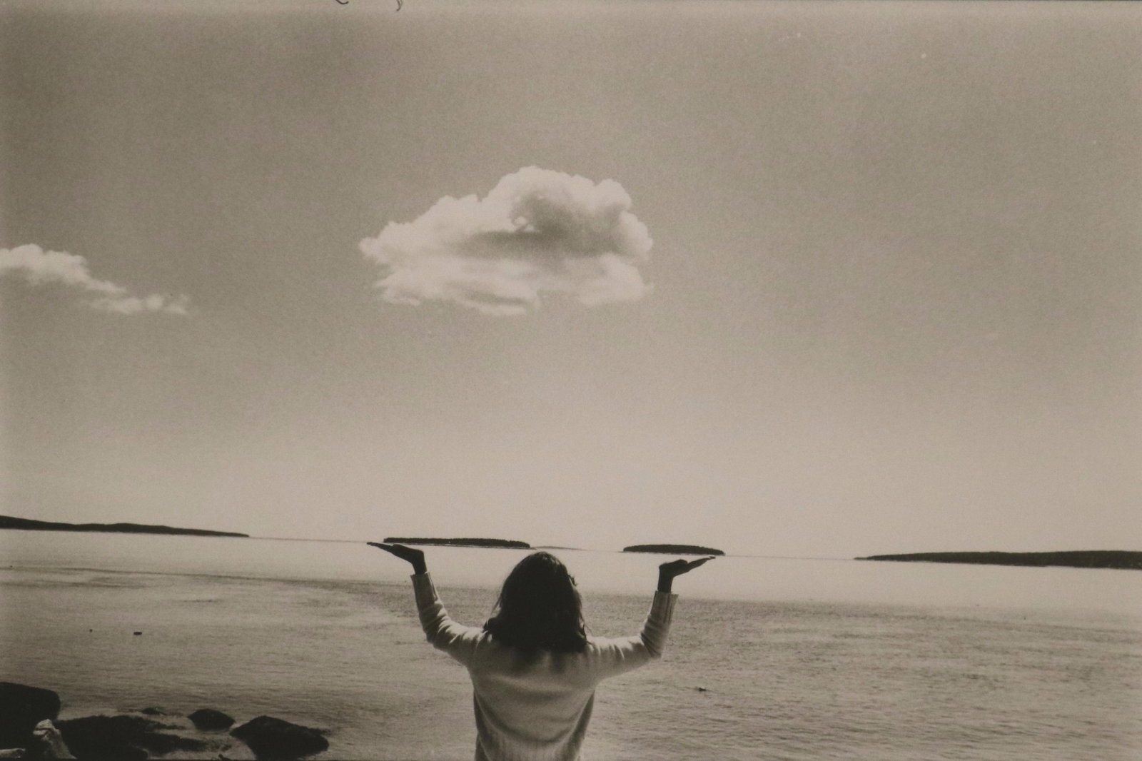 LINN SAGE, (American Born 1937). Cloud Bearer, Sight (as matted): 6 x 8.5 inches; frame: 14 x 18: LINN SAGEAmerican, Born 1937Cloud BearerPlayful black and white photograph of the subject’s hands with a floating cloud, creating a sense of connection between the human figure and the vast landscap