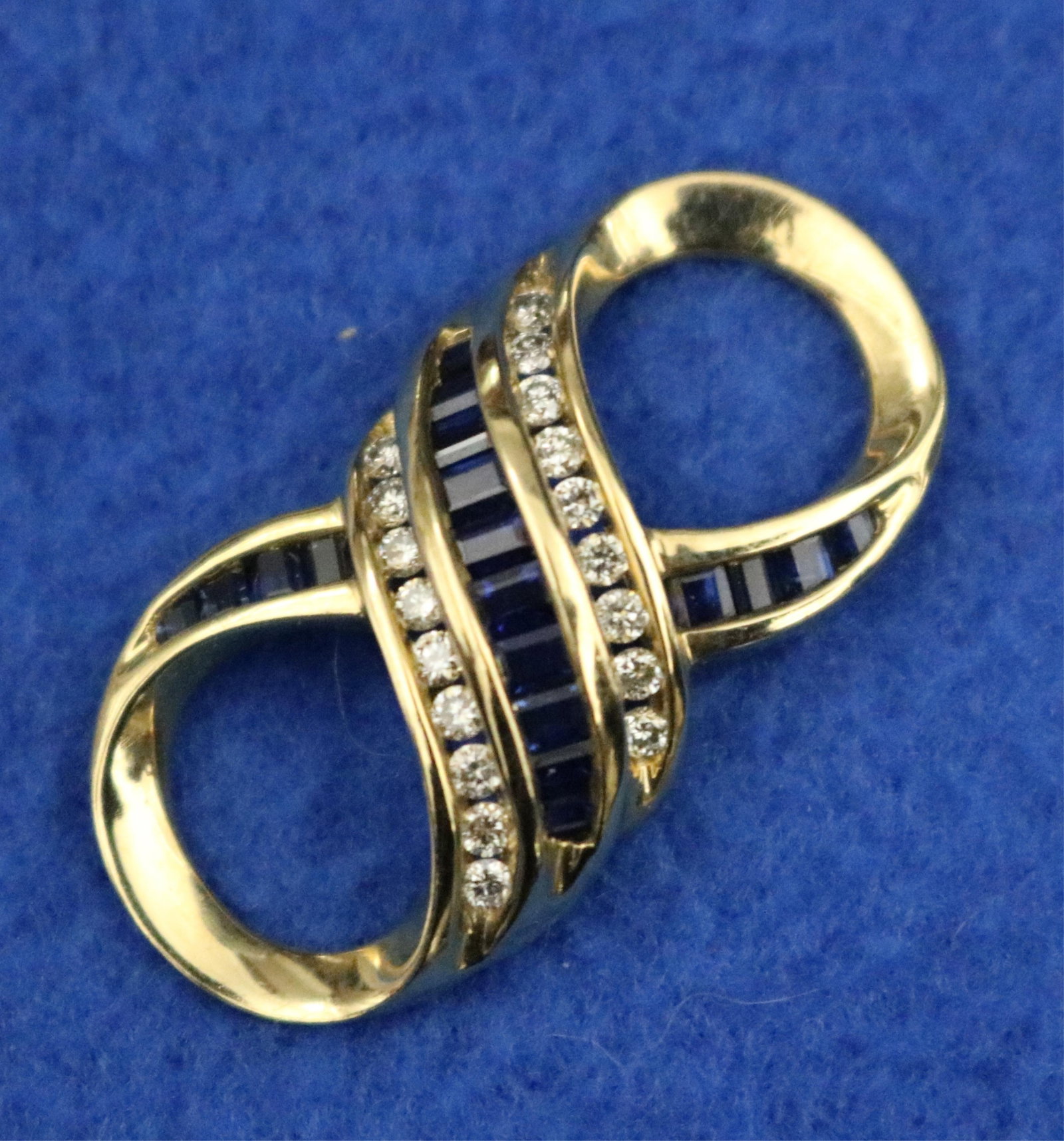 14K YELLOW GOLD DIAMOND AND SAPPHIRE PENDANT/NECKLACE ENHANCER - L: 1 1/4 in. Gross wt. 3 dwt.: 14K YELLOW GOLD DIAMOND AND SAPPHIRE PENDANT/NECKLACE ENHANCER Figure-eight design channel-set with 18 matched brilliant-cut round diamonds and 18 graduated sapphire baguettes L: 1 1/4 in. Gross wt. 3