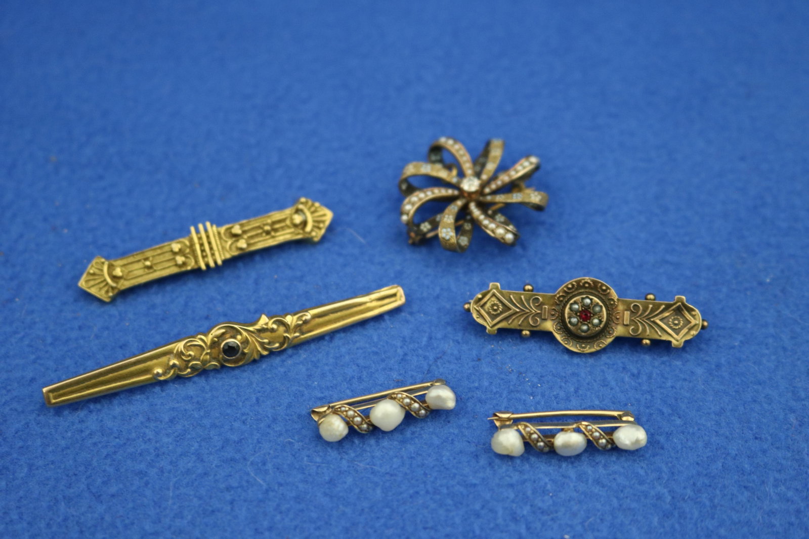 SIX ASSORTED GOLD PINS, FIVE SET WITH VARIOUS GEMSTONES late 19th-early 20th century - Gross wt.: 14: SIX ASSORTED GOLD PINS, FIVE SET WITH VARIOUS GEMSTONES late 19th-early 20th century Including looped ribbon sunburst with seed pearls and enameled decoration centering .15ct. Old Mine cut diamond,