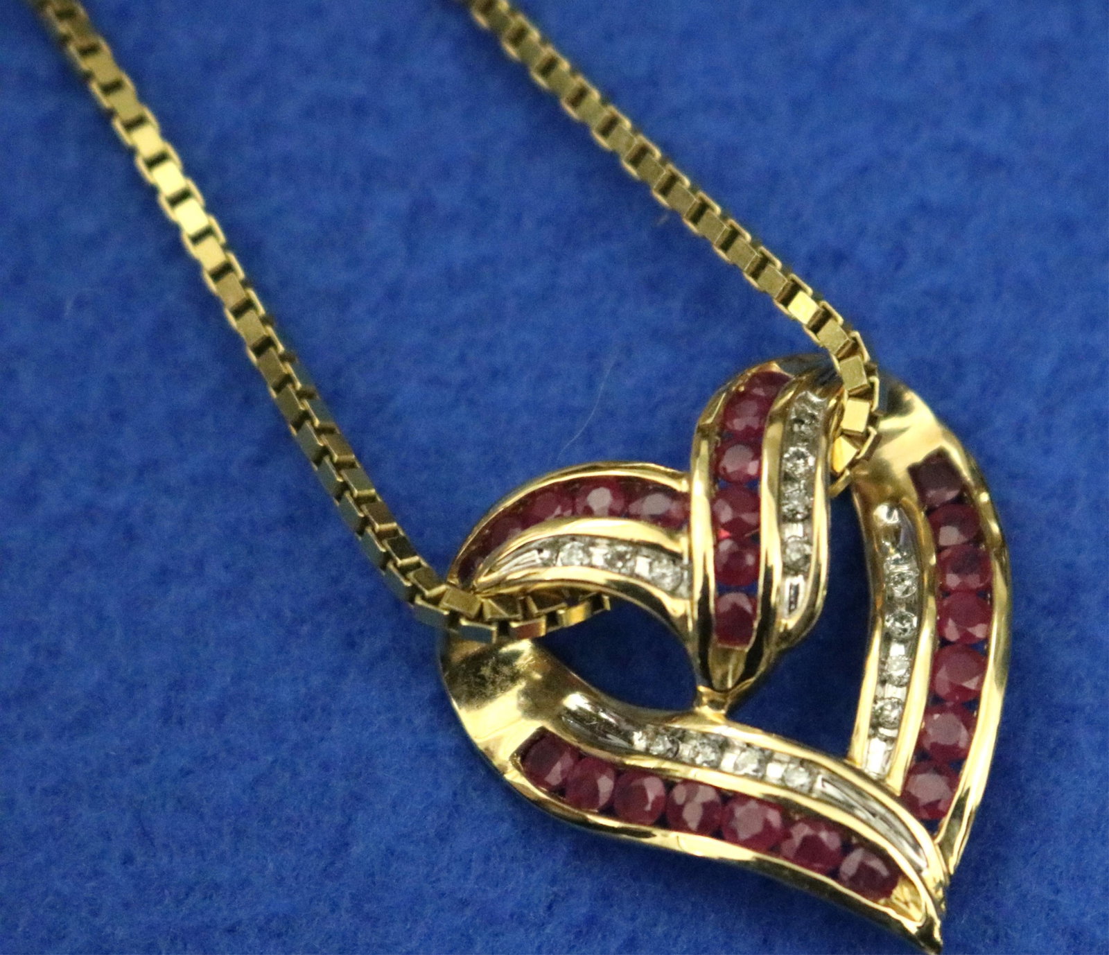 14K BRIGHT-POLISHED YELLOW GOLD, RUBY AND DIAMOND HEART-SHAPE PENDANT SUSPENDED ON 14K BOX-LINK: 14K BRIGHT-POLISHED YELLOW GOLD, RUBY AND DIAMOND HEART-SHAPE PENDANT SUSPENDED ON 14K BOX-LINK CHAIN Scrolling heart with open center set with four channels of 25 round rubies and four channels of 15