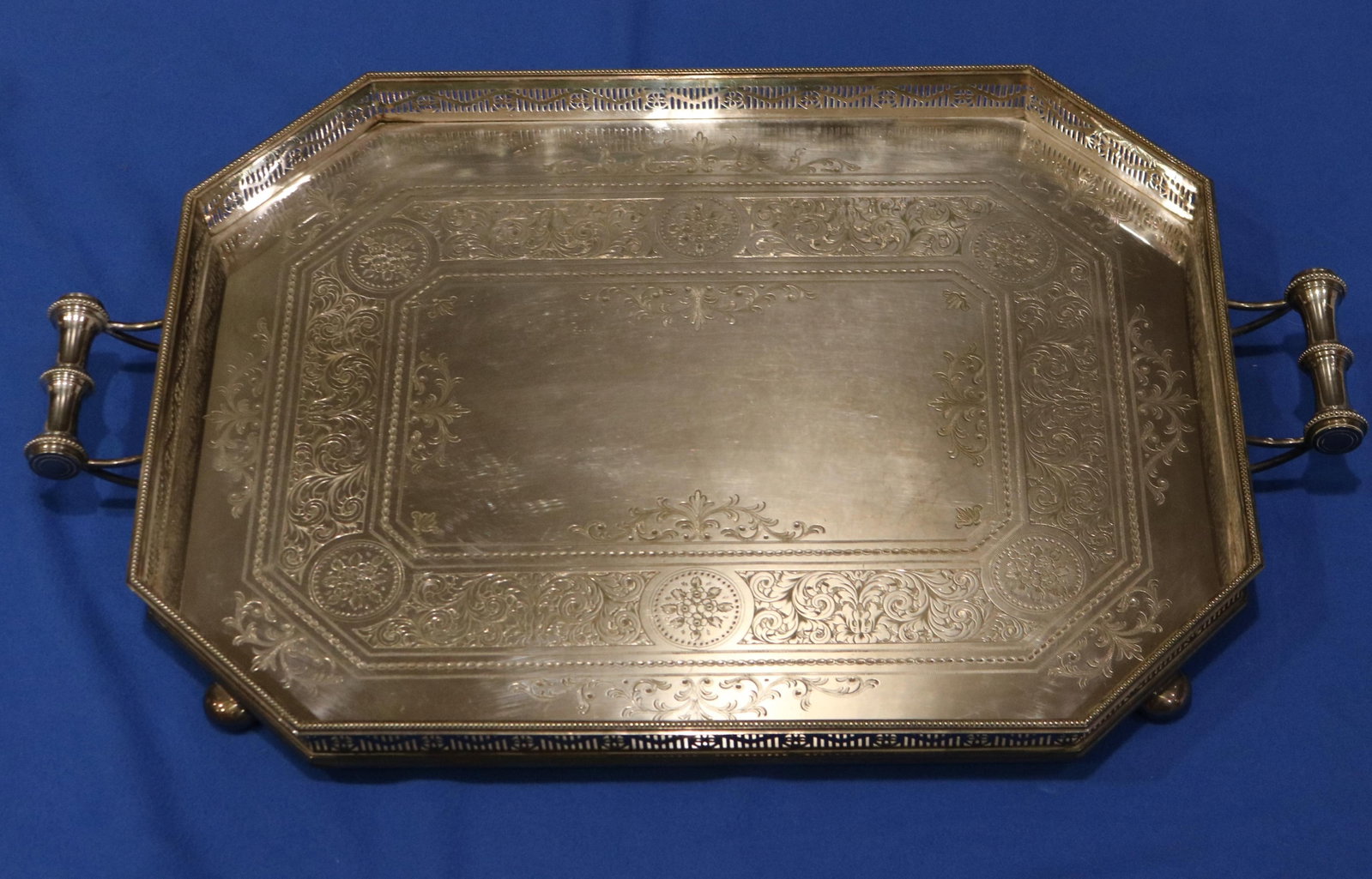 HEAVY SILVER PLATED SERVING TRAY late 19th century - Between handles, 22 in. 16 3/4 in..: HEAVY SILVER PLATED SERVING TRAY late 19th century Rectangular with canted corners; pierced gallery; chased center; projecting handles; raised on four bun-form feet Between handles, 22 in. 16 3/4 in.