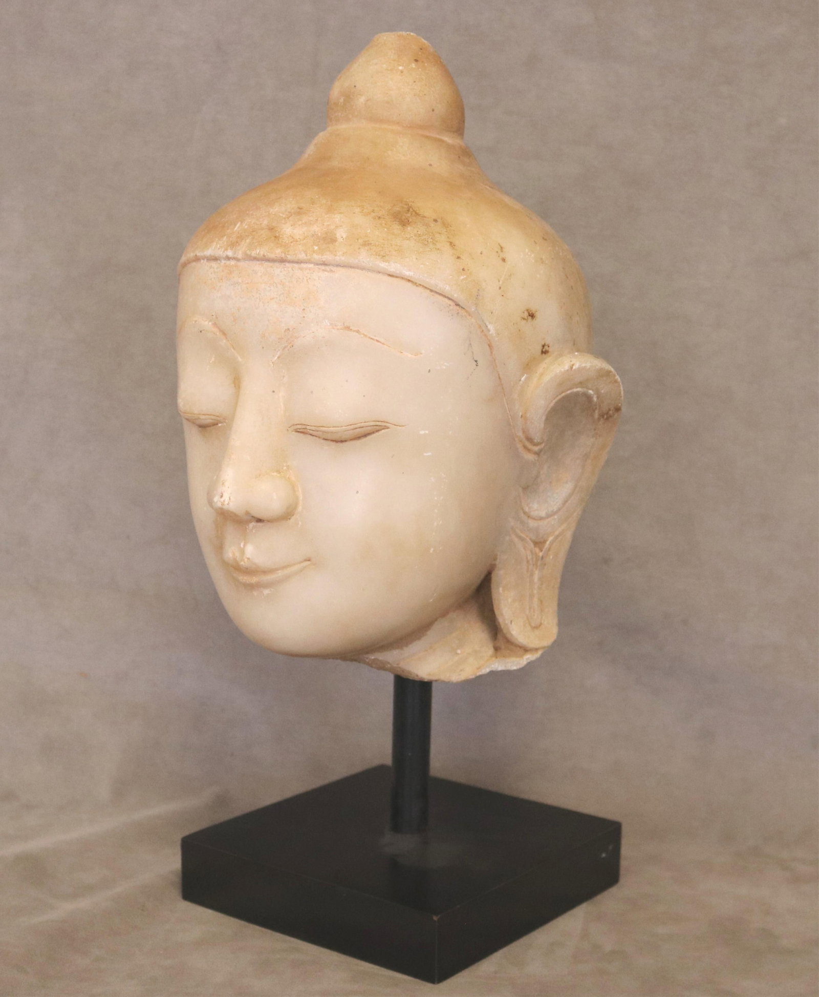 BURMESE MANDALAY ALABASTER MARBLE BUDDHA HEAD - H: 13 1/2 in. (head only); 19 in. including base..: BURMESE MANDALAY ALABASTER MARBLE BUDDHA HEAD Sculptural fragment carved in classic Mandalay style. Mounted on square black metal display stand. H: 13 1/2 in. (head only); 19 in. including base.