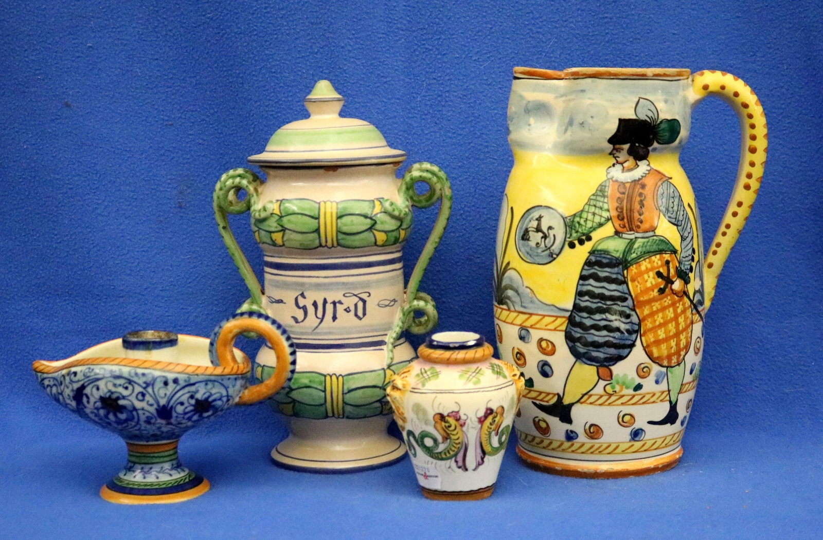 FOUR ASSORTED PIECES VINTAGE ITALIAN HAND DECORATED MAJOLICA POTTERY - .: FOUR ASSORTED PIECES VINTAGE ITALIAN HAND DECORATED MAJOLICA POTTERY Including large lidded apothecary jar with twin handles inscribed "Syrd" in Gothic script; tall pitcher with yellow background depi
