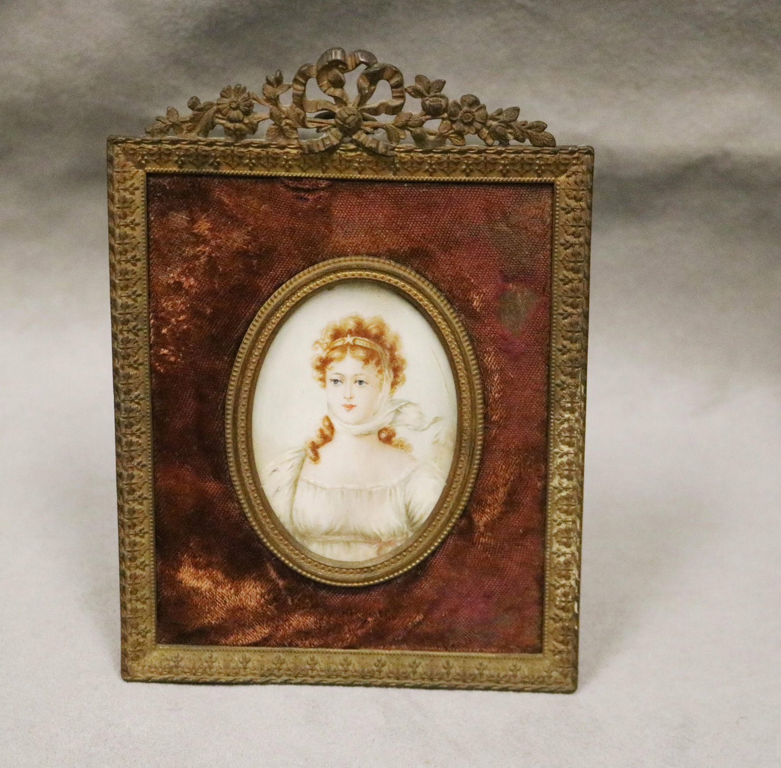 ARTIST UNKOWN (19th century). LADY IN WHITE EMPIRE STYLE DRESS, Miniature: 2 5/8 in. x 1 7/8 in.: ARTIST UNKOWN 19th century LADY IN WHITE EMPIRE STYLE DRESS Signed illegibly at right, "L[?]" Watercolor, in the oval. 19th century gilt-metal easel-back frame. Miniature: 2 5/8 in. x 1 7/8 in.