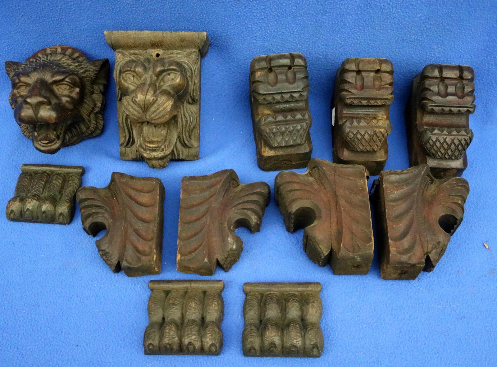 COLLECTION OF TWELVE HAND-CARVED WOODEN ARCHITECTURAL ELEMENTS INTENDED AS DECORATIVE FURNITURE: COLLECTION OF TWELVE HAND-CARVED WOODEN ARCHITECTURAL ELEMENTS INTENDED AS DECORATIVE FURNITURE ORNAMENTS Including two lion masks rendered with expressive facial features.