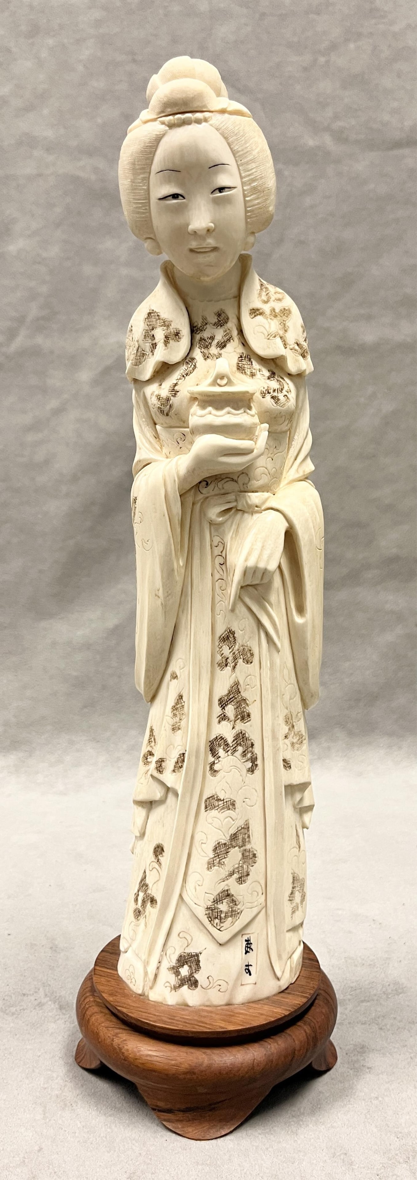 CHINESE CARVING OF STANDING KWAN YIN HOLDING VESSEL - H: 14 1/2 in., with stand.: CHINESE CARVING OF STANDING KWAN YIN HOLDING VESSEL Scrimshaw highlights. On teakwood stand. H: 14 1/2 in., with stand PROVENANCE: ?Merry Hill?, an historic mansion built in 1899 and located in Greens