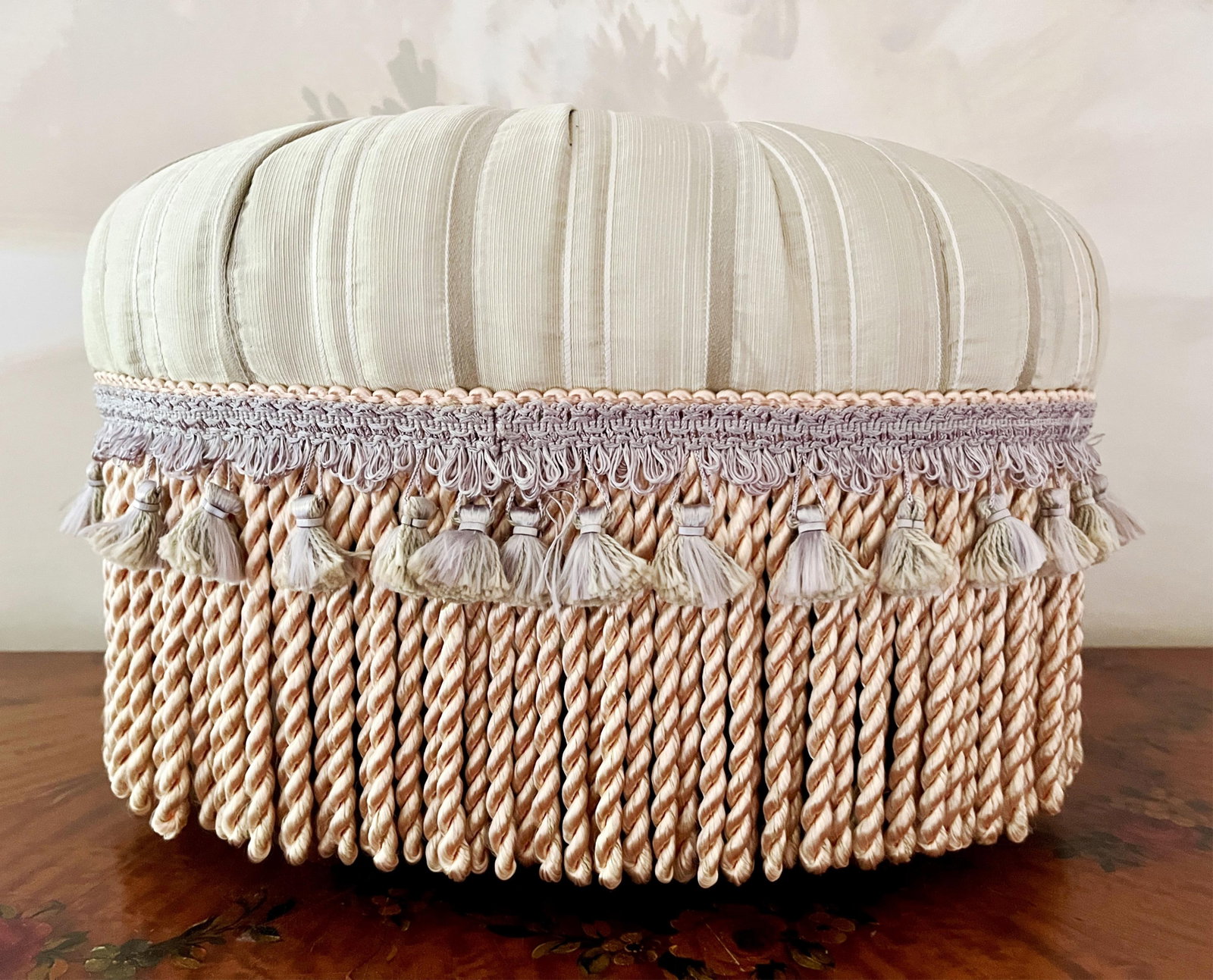 UPHOLSTERED OVAL POUF-STYLE FOOT STOOL WITH TASSELS AND FRINGE - H: 10 IN; W: 15 IN; D: 12 IN. (1 of 2)
