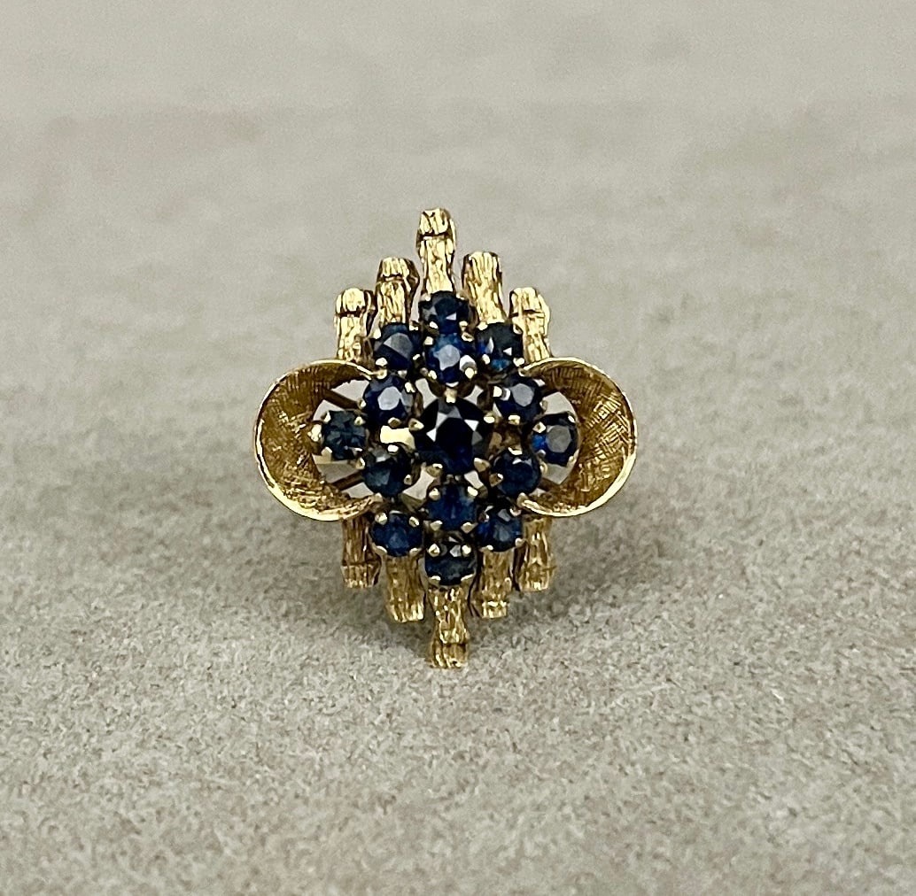 14K (585) YELLOW GOLD AND SAPPHIRE OPENWORK GEOMETRIC DESIGN RING Domed cluster of 15 round: 14K (585) YELLOW GOLD AND SAPPHIRE OPENWORK GEOMETRIC DESIGN RING Domed cluster of 15 round sapphires centered on bark-textured bars and two textured crescent motifs. Ring size: 6. Gross wt: 3 dwt.