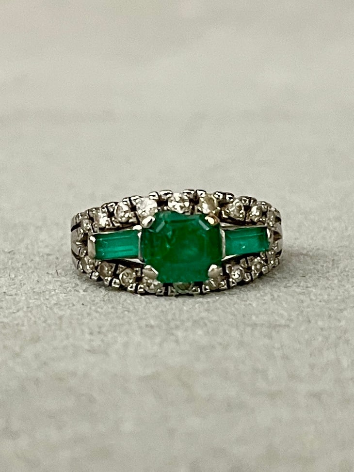 18K WHITE GOLD AND DIAMOND AND EMERALD TAPERING BAND Horizontally-oriented emerald cut emerald: 18K WHITE GOLD AND DIAMOND AND EMERALD TAPERING BAND Horizontally-oriented emerald cut emerald raised and flanked by two rectangular emerald baguettes, centered by two rows of total of 18 round diamon