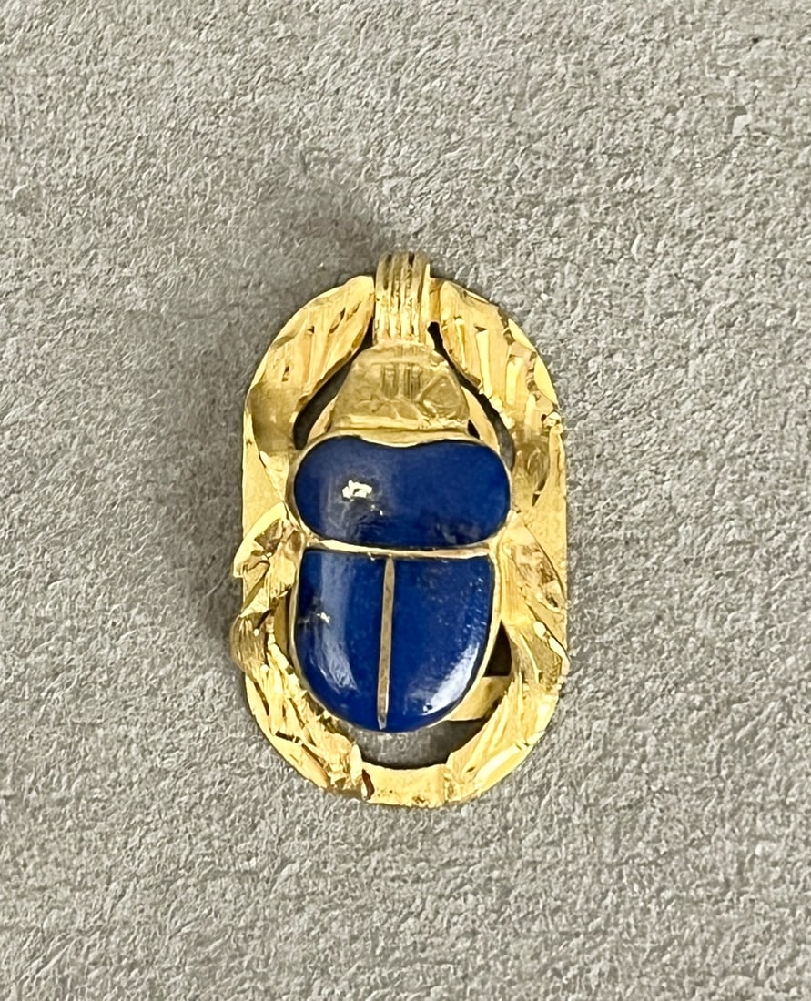 18K TEXTURED YELLOW GOLD AND LAPIS LAZULI SCARAB DESIGN PENDANT Openwork oval pendant centers: 18K TEXTURED YELLOW GOLD AND LAPIS LAZULI SCARAB DESIGN PENDANT Openwork oval pendant centers bezel-set raised lapis scarab. L: 1 1/4". Gross Wt: 6 dwt.
