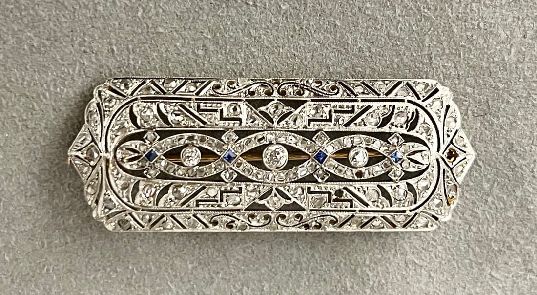 EDWARDIAN PLATINUM-ON-YELLOW GOLD, DIAMOND, AND SAPPHIRE OBLONG OPENWORK BROOCH Scrolling and: EDWARDIAN PLATINUM-ON-YELLOW GOLD, DIAMOND, AND SAPPHIRE OBLONG OPENWORK BROOCH Scrolling and geometric decoration set with numerous old mine cut and rose cut diamonds and four square-cut sapphires. L