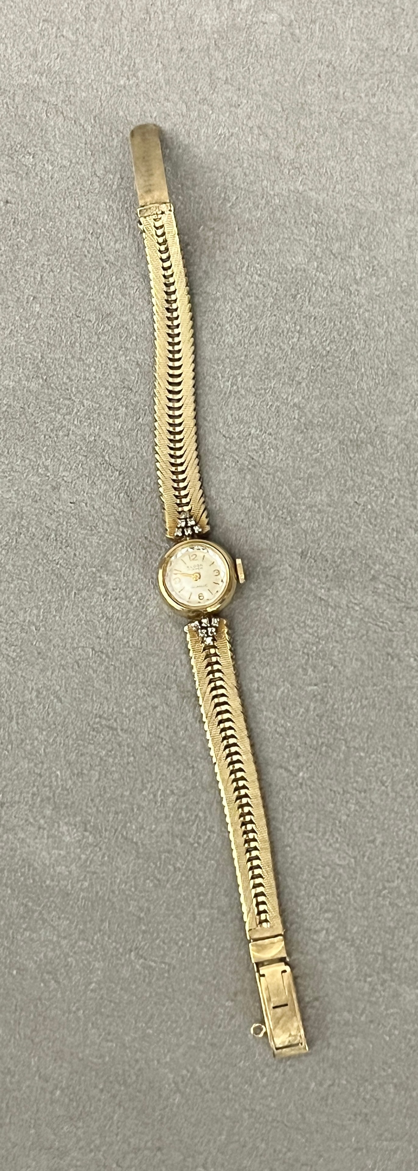 LADY'S 14K (585) YELLOW GOLD WRISTWATCH BY ELOGA Circular case with silvered dial having gold bars: LADY'S 14K (585) YELLOW GOLD WRISTWATCH BY ELOGA Circular case with silvered dial having gold bars for indices, centered by two clusters of six round diamond accents; tapering, textured yellow gold fl