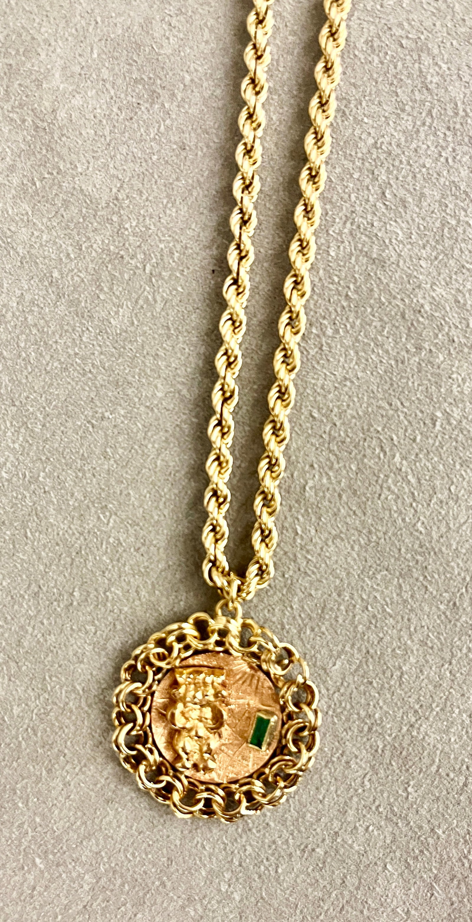 COLOMBIAN 18K YELLOW GOLD AND EMERALD MEDALLION SUSPENDED ON 14K YELLOW GOLD ROPE CHAIN Medallion: COLOMBIAN 18K YELLOW GOLD AND EMERALD MEDALLION SUSPENDED ON 14K YELLOW GOLD ROPE CHAIN Medallion has applied figure of Aztec god on textured ground with bezel-set rectangular emerald; chain-link bord