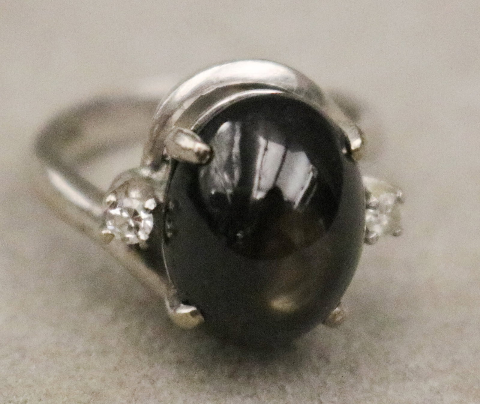 18K WHITE GOLD, DIAMOND AND BLACK STAR SAPPHIRE CABOCHON RING - Ring size: 5 1/4. Gross wt. 4 dwt..: 18K WHITE GOLD, DIAMOND AND BLACK STAR SAPPHIRE CABOCHON RING Oval cabochon centered by two brilliant-cut round diamonds on shoulders of shank Ring size: 5 1/4. Gross wt. 4 dwt.